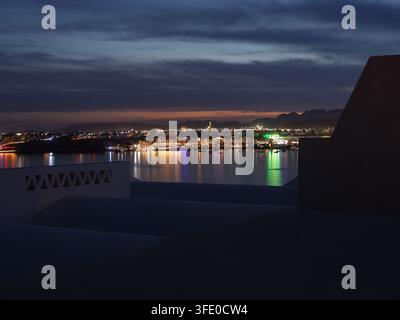 Vista notturna di Sharm el Sheikh, Egitto, con luci che si riflettono sul Mar Rosso e montagne che si stagliano contro il cielo serale Foto Stock