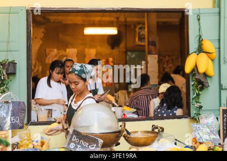 Venditore di strada di Bangkok che serve i clienti in un negozio di mango con fronte aperto Foto Stock