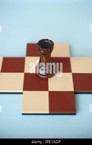 Prima vista di un alfiere di legno scuro in piedi su una piccola croce di scacchi rossa e crema su uno sfondo blu pallido Foto Stock