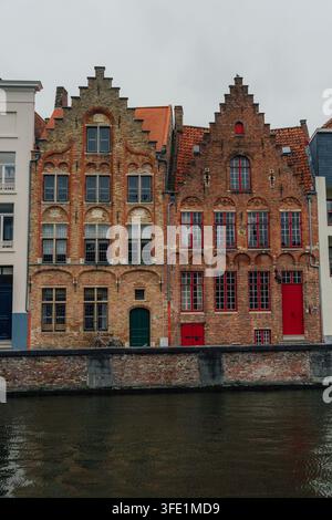 Bruges, Belgio – 03 febbraio 2024: Vista di case tradizionali in mattoni con frontoni a gradini e tetti di tegole rosse che costeggiano il canale nel centro storico della città Foto Stock