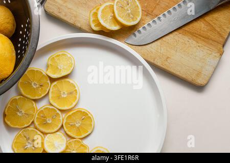 Limoni freschi di giardino affettati per l'essiccazione su un piatto bianco vicino a un tagliere di legno e a un cesto con limoni Foto Stock