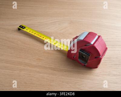 Nastro metrico rosso esteso sul legno - Un nastro metrico retrattile rosso e grigio completamente esteso su una superficie di legno chiaro, con segnature metriche. Foto Stock
