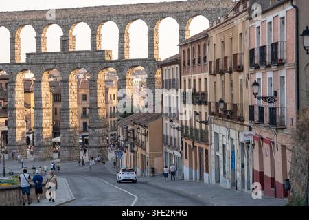 L’acquedotto romano storico si erge su una stretta strada acciottolata a Segovia, in Spagna, incorniciato dalla luce calda della sera, dai balconi e dalle facciate in arenaria, con Foto Stock