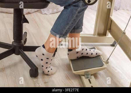 Piedi femmina sul pedale di una macchina da cucire, primo piano del motore Foto Stock