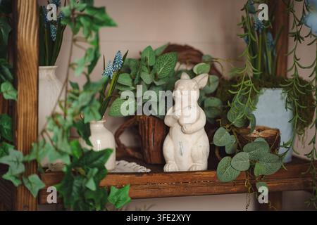 Una composizione decorativa su un tavolo di legno. Due figurine di conigli stanno accanto a vasi di giacinti bianchi e blu, un annaffiatoio e piantine in torba Foto Stock