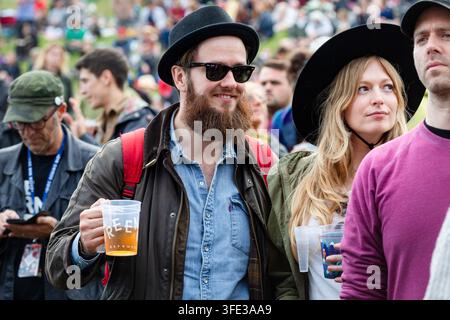 UOMO E DONNA STILEVOSE NELLA FOLLA DEL FESTIVAL, REPORTAGE, GREEN MAN FESTIVAL 2017, BRECON, GALLES, REGNO UNITO, 2017: Un uomo barbuto elegante con cappello e occhiali da sole che tiene una birra è in piedi con una donna, anch'ella con cappello, che osserva da una grande folla del festival. Foto: Rob Watkins. INFO: Il Green Man Festival è iniziato nel 2003 in Galles. Si tiene ogni anno nei Brecon Beacons nel terzo fine settimana di agosto e celebra musica alternativa, arte, letteratura, scienza e cultura a misura di famiglia in uno splendido scenario montano. Foto Stock