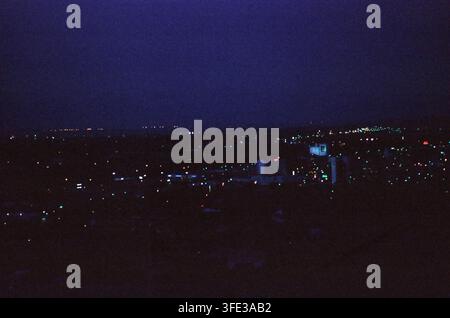 Vista notturna elevata di una città tentacolare con luci sparse che luccicano contro un cielo blu-nero profondo, creando una scena atmosferica suggestiva. Foto Stock