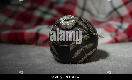 Primo piano di una elegante bacchetta di albero di Natale nera scura con motivo di ramo di felce scintillante oro su coperta di peluche bianca, tessuto tartan a quadri rossi b Foto Stock