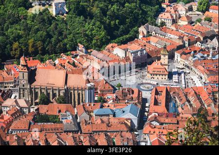 Vista aerea della vecchia città di Brasov con la Chiesa Nera e la Piazza del Consiglio dai tetti rossi circondati da colline boschive verdi, Brasov, Transilvania, Romania Foto Stock