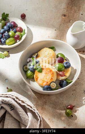 Pancake di formaggio cottage syrniki, frittelle di ricotta con latte condensato e bacche fresche per la colazione alla luce chiara del mattino Foto Stock
