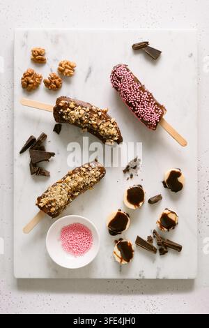 Banane surgelate e lecci di cioccolato con noci e spruzzi rosa. Dolci vegani fatti in casa. Vista dall'alto. Foto Stock