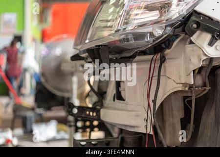 Cablaggio esposto dei fari dell'auto e componenti della carrozzeria anteriore durante la riparazione e la manutenzione automobilistica in un'officina professionale per veicoli Foto Stock