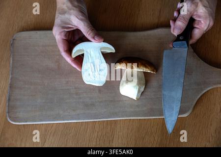 Un primo piano dettagliato di una chef che tiene nella mano una metà di fungo porcini fresco tagliato e un coltello da cucina nell'altra mano. Foto Stock