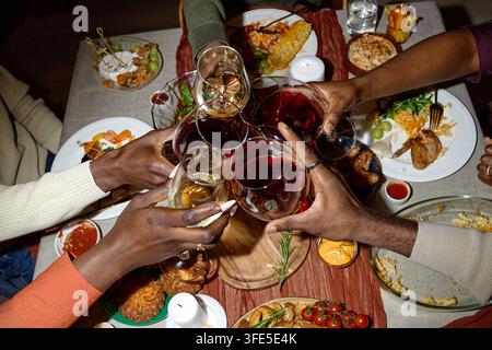 Amici neri che brindano con bicchieri di vino sopra un tavolo da cena festivo delle feste Foto Stock