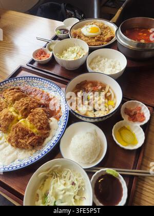 Un pasto tradizionale coreano con cotoletta fritta con uovo, riso, zuppa, insalata, kimchi e sottaceti serviti su vassoi di legno in Corea. Foto Stock
