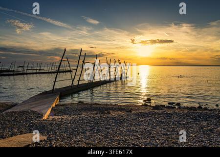 Tramonto sul molo di Pebble Beach con pali di legno che si riflettono sul mare calmo e nella luce dorata, Savudrija Foto Stock