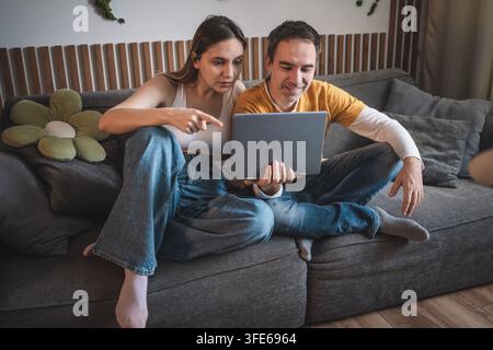 Coppia concentrata che guarda insieme lo schermo di un laptop, la donna indica seriamente. Discutendo di lavoro, pianificazione e concentrazione condivisa sul scr Foto Stock