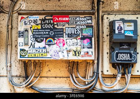 Scatola elettrica e contatore da un lato e adesivi graffiti e fili dall'altro che creano una collage di arte urbana su un muro sporco a Omoide Yokocho. Foto Stock