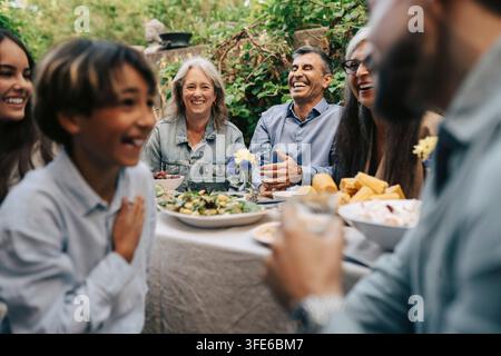 Memri della famiglia allegri che godono di un pasto pomeridiano soleggiato seduti nel cortile posteriore Foto Stock