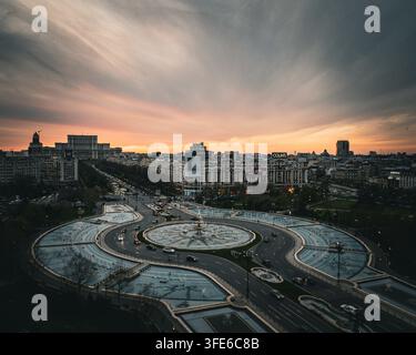 Vista aerea del Palazzo del Parlamento e delle fontane illuminate in Piazza Unirii durante un tramonto drammatico nel centro città di Bucarest, B Foto Stock
