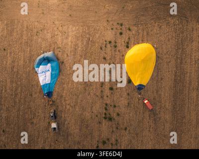 Veduta aerea di due mongolfiere, una blu e bianca e l'altra gialla, posate su un campo secco a Gravina in Puglia, Puglia, Italia. Foto Stock