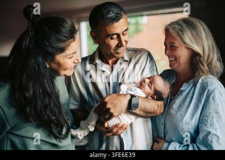 Uomo anziano felice che tiene un neonato addormentato circondato da due donne sorridenti Foto Stock