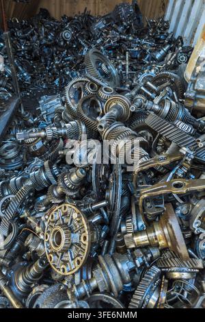 Prima vista di un grande e caotico mucchio di vari componenti meccanici metallici, inclusi ingranaggi e parti di trasmissione. I materiali scuri e unti suggeriscono che si tratta di oggetti di recupero destinati al riciclo. Foto Stock
