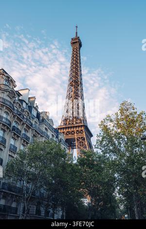 Torre Eiffel a Parigi tra edifici residenziali storici in stile Haussmann e cime degli alberi verdi contro un cielo blu leggermente nuvoloso, Parigi, Île-de-France Foto Stock