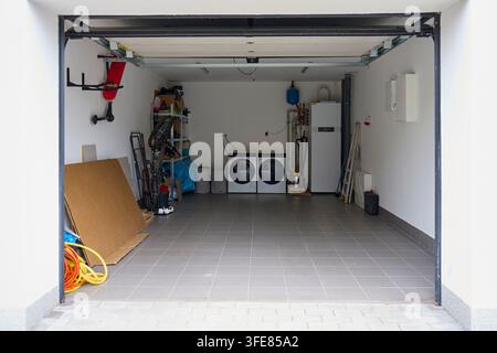 Garage aperto con lavatrice, asciugatrice, scaffali, attrezzi e attrezzature domestiche. Area di stoccaggio e lavanderia residenziale Foto Stock