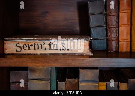 Volume manoscritto di sermone antico appoggiato su uno scaffale di biblioteca in legno accanto a libri in pelle nel castello di Peñíscola. Foto Stock