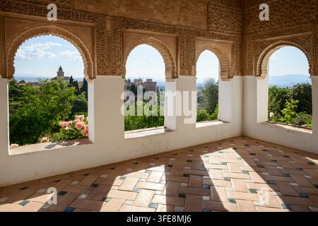 I giardini del palazzo Generalife visti attraverso archi moreschi del complesso dell'Alhambra a Granada, Andalusia, Spagna, durante un pomeriggio di primavera soleggiato. Foto Stock