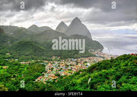 Vista aerea della città di Soufriere e delle iconiche montagne dei Pitons circondate da una lussureggiante foresta tropicale e dall'oceano a Santa Lucia. Foto Stock