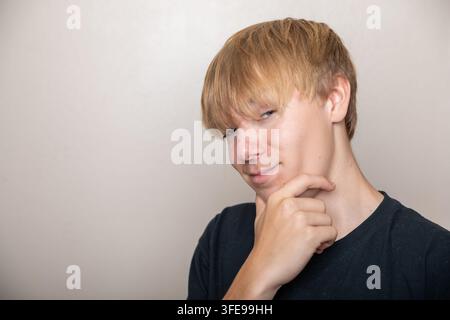 Un giovane con i capelli biondi guarda la fotocamera con un'espressione perplessa Foto Stock