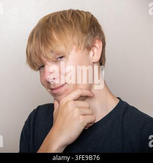 Un giovane con i capelli biondi guarda la fotocamera con un'espressione perplessa Foto Stock