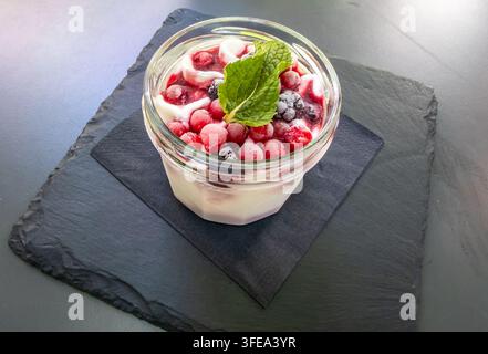 Barattolo di vetro pieno di parfaits di yogurt alle bacche salutari, con strati cremosi, frutta congelata e una guarnizione di menta fresca Foto Stock