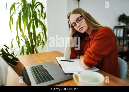 Giovane donna adulta che si sente esausta e stressata mentre lavora da remoto da casa Foto Stock