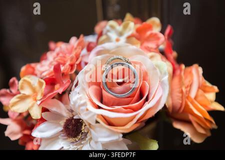 Prima vista di anelli nuziali incastonati in un delicato mazzo di rose bianche e pesche. Foto Stock