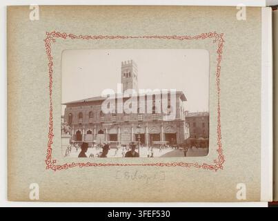 Una fotografia di un grande edificio in pietra con finestre ad arco e una torre centrale, situata a Bologna, in Italia, con diverse piccole figure in piedi o che camminano davanti, di Jean-Charles Chaufour, un fotografo francese, nel 1900, come parte di una serie intitolata "Recueil. Voyage en Italie". Foto Stock
