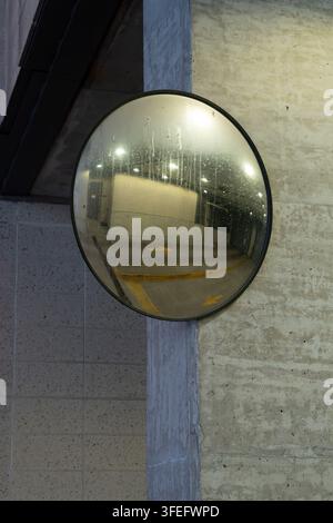 Foto verticale di uno specchio convesso per il traffico installato vicino all'uscita di un garage, che offre un ampio campo visivo a conducenti e pedoni Foto Stock
