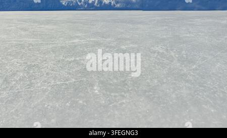 una vasta distesa naturale di ghiaccio. Texture superficiale di ghiaccio graffiata. Sfondo di ghiaccio blu con tracce di pattinaggio, crepe, graffi. Retro ruvido della pista da ghiaccio per sport invernali Foto Stock