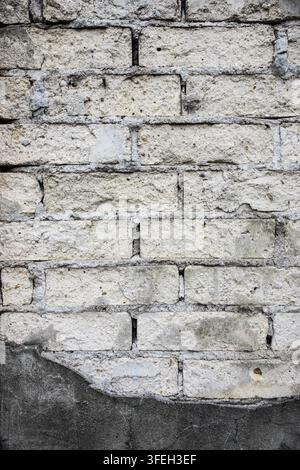 muro di muratura eroso con mattoni chiari, malta danneggiata e intonaco grigio screpolato, che mostra decadimento, riparazione e texture invecchiata dell'edificio Foto Stock