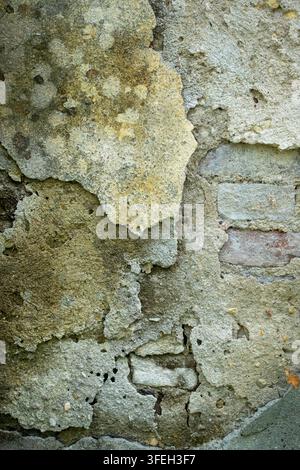 L'intonaco giallo che si sfalda rivela il cemento grigio ruvido sottostante, creando una texture di parete invecchiata e distrutta con crepe, macchie e degrado Foto Stock