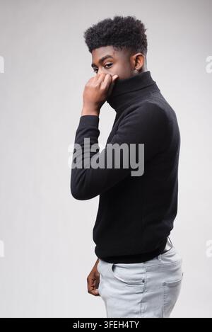 Giovane uomo nero con maglione a collo alto nero e jeans chiari Foto Stock