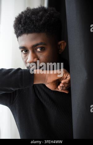 Giovane uomo nero con acconciatura afro che guarda pensieroso nel vuoto Foto Stock