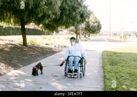 Donna su sedia a rotelle porta a spasso il suo cane nel parco Foto Stock