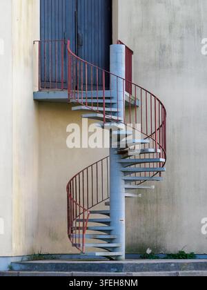 Scalinata a chiocciola in cemento attaccata all'esterno di un edificio, con una ringhiera in metallo rosso arrugginita che conduce a una porta di legno chiusa Foto Stock