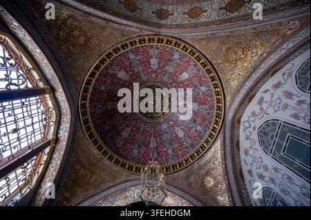 Istanbul, Turchia, 3 agosto 2025. Motivi dorati intricati e mosaici colorati adornano una grande cupola e un soffitto ad arco in un interno imperiale ottomano Foto Stock