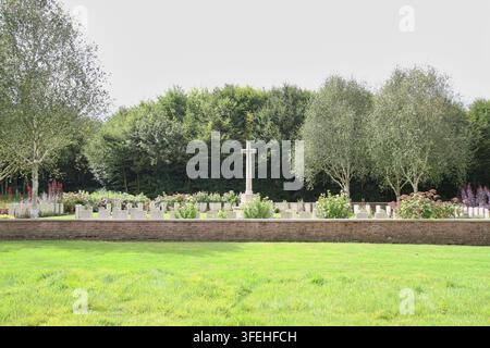 La croce bianca in pietra del Sacrificio si erge tra file di lapidi dietro un basso muro di contenimento in mattoni in un cimitero militare del Commonwealth in Belgio. Foto Stock