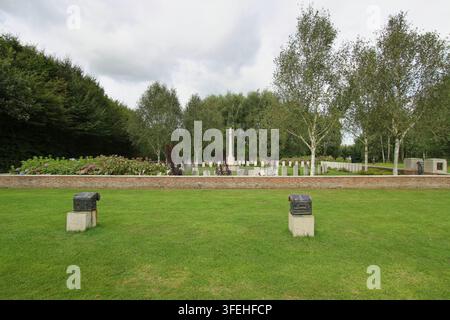 La croce bianca in pietra del Sacrificio si erge tra file di lapidi dietro un basso muro di contenimento in mattoni in un cimitero militare del Commonwealth in Belgio. Foto Stock