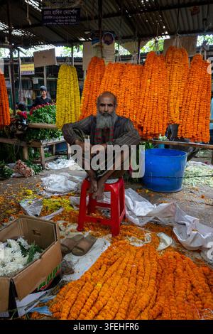 Vecchio venditore seduto su uno sgabello tra ghirlande di calendule arancioni e gialli in un mercato dei fiori, Divisione di Dhaka, Dhaka, Bangladesh Foto Stock
